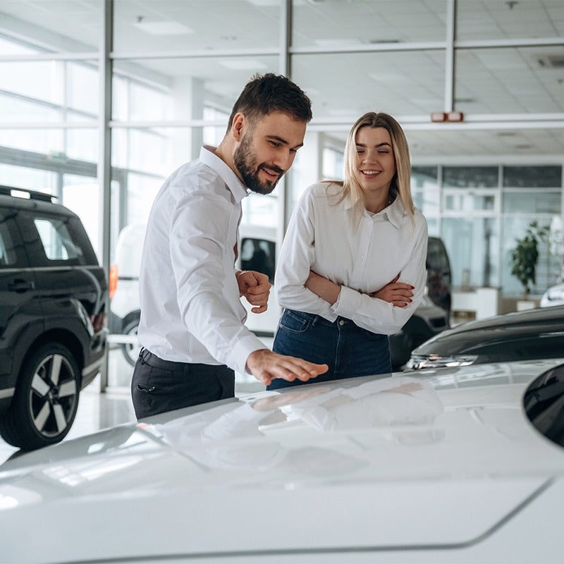 A GMC sales professional shows a long-haired blonde woman around the selection of vehicles in a sunlit GMC showroom.